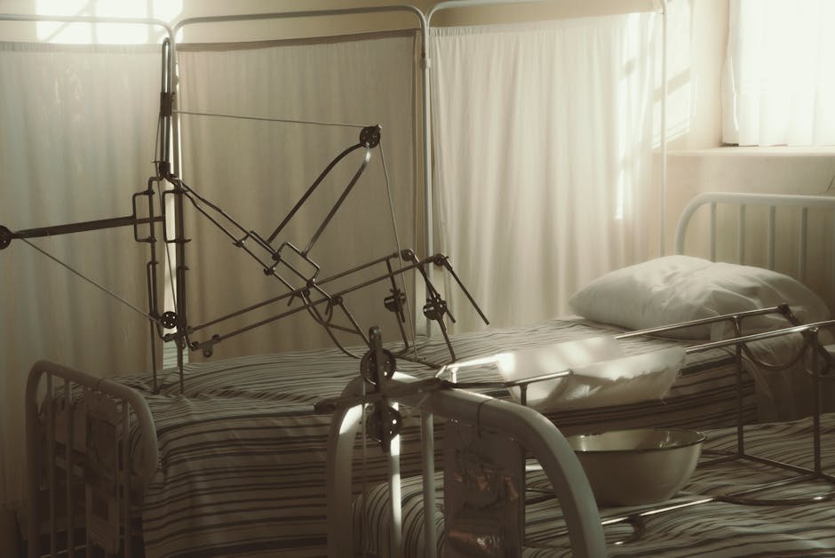 An empty hospital bed surrounded by medical equipment in a quiet, sunlit room.
